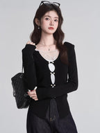 Woman wearing a black long-sleeved top with white lace trim and decorative buttons, carrying a black quilted handbag.