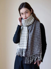 Woman wearing a black long-sleeve top and a plaid scarf with fringe detail, styled loosely around her neck.