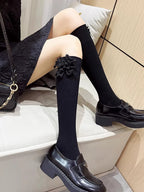 Black knee-high socks with decorative flower accents worn with black loafers.