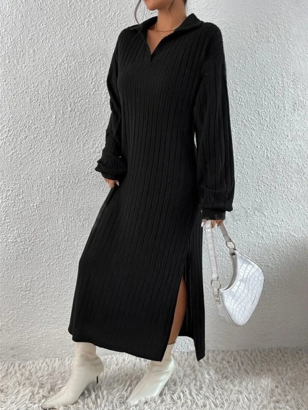 Woman wearing a black long-sleeved ribbed knit dress with a high slit and white boots, holding a white handbag.