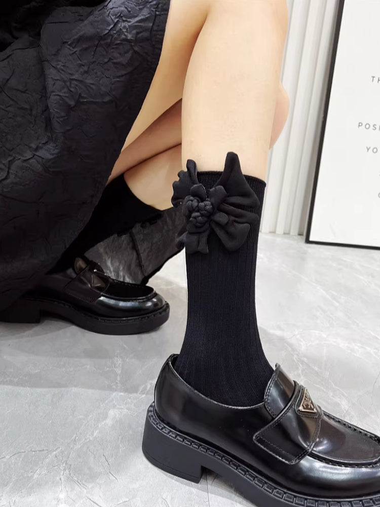 A person's legs showing black knee-high socks with a textured flower detail.
