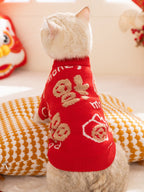 The back of a white cat wearing a red knit sweater with gold Chinese character designs.