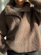 Full body shot of a woman in a brown fleece pullover and dark wash jeans.