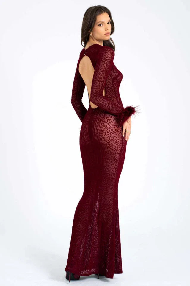 Woman wearing a long-sleeved, burgundy, animal print, sheer mesh dress with feathered cuffs and an open back, back three-quarter view.
