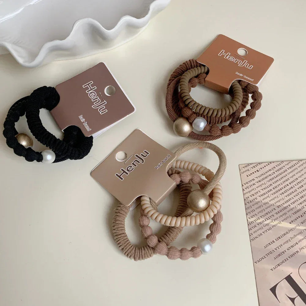 Overhead view of three sets of coiled hair ties in black, brown, and beige, featuring pearl and metallic bead details.