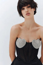Close-up of a model wearing a black strapless dress with heart-shaped embellishments on the bust and a corset bodice.