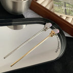 Two hairpins, one gold-tone and one silver-tone, rest on a mirrored tray.