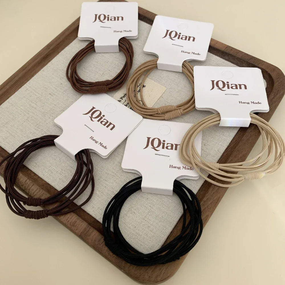 Several packs of JQian elastic hair ties, including black, brown, and beige, laid out on a wooden surface.