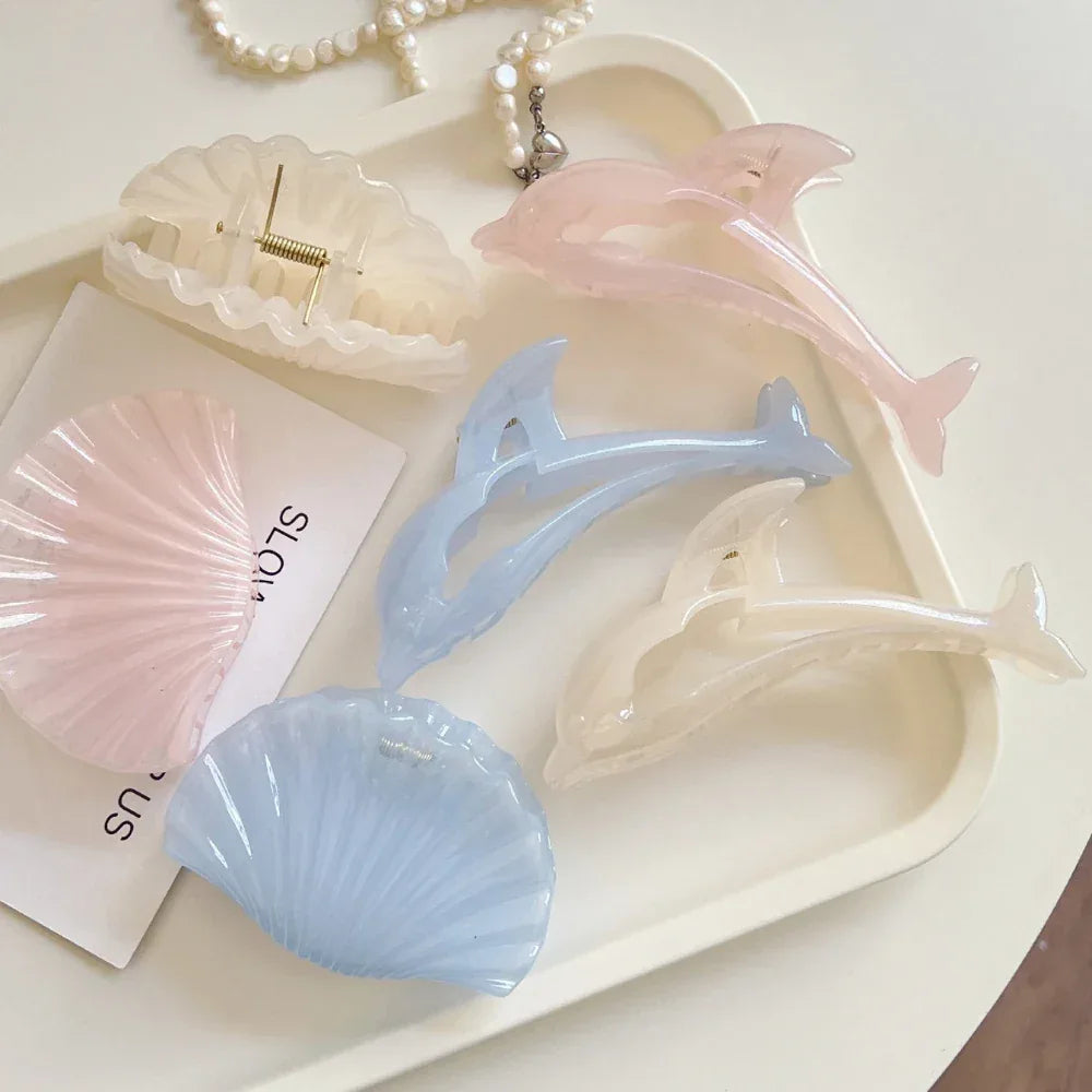 Assortment of pastel dolphin and seashell hair claw clips arranged on a white tray