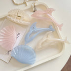 Assortment of pastel dolphin and seashell hair claw clips arranged on a white tray