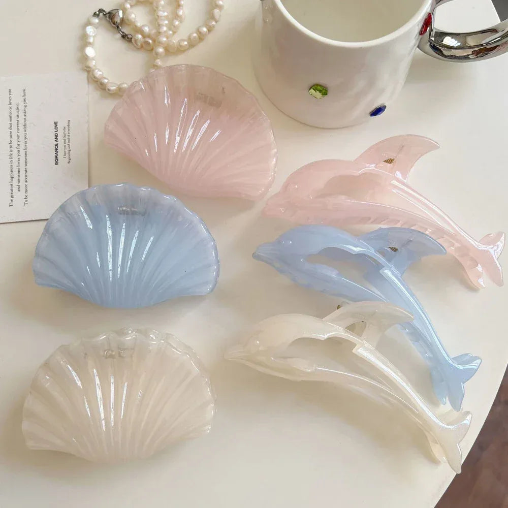Collection of pastel colored dolphin and seashell hair claw clips and a pearl necklace on a white surface