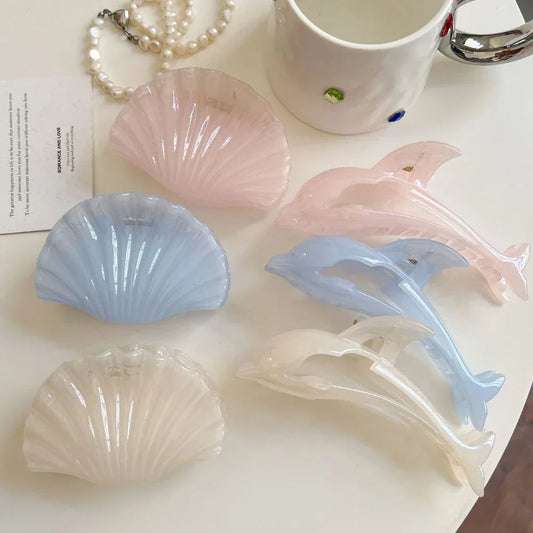 Collection of pastel colored dolphin and seashell hair claw clips and a pearl necklace on a white surface