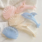 Various pastel dolphin and seashell hair claw clips scattered on a white fabric and table