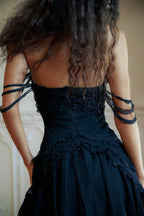 Back view of a model wearing a black strapless mini dress with ruffle trim and sheer tiered skirt, showing detail on the back.