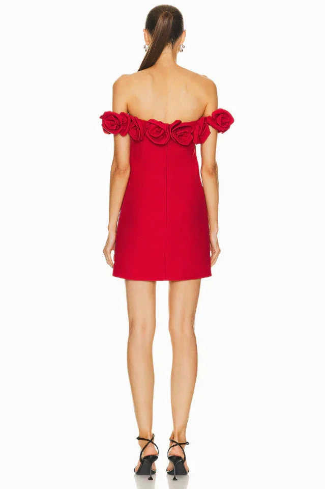 Back view of a woman wearing a red off-the-shoulder mini dress with rose embellishments on the neckline and black strappy heels.