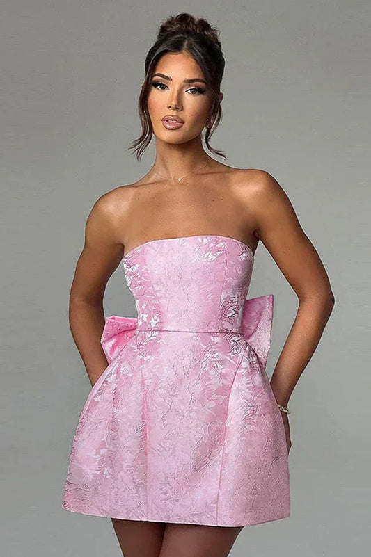 Model wearing a pink strapless mini dress with a large bow on the back.