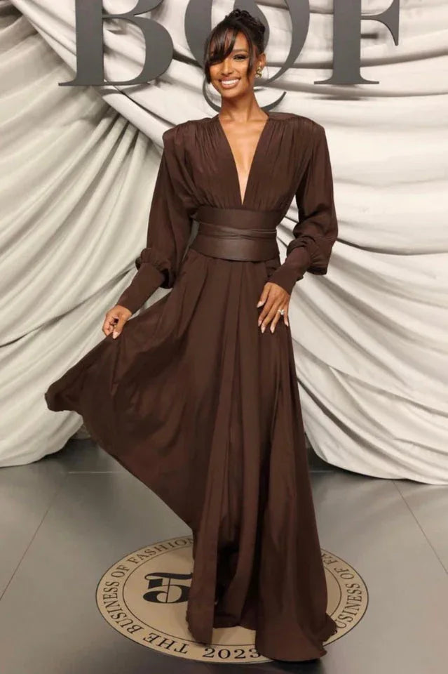 A model poses in a flowing brown maxi dress with a V-neckline and a wide waist belt. Main image