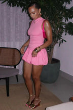 Woman wearing a pink sleeveless dress with a bubble hem skirt and gold wedge sandals.