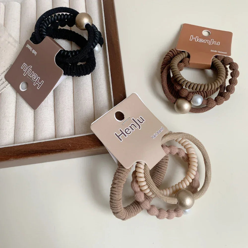 A flat lay of three sets of hair ties, including black, brown, and beige options, each with decorative beads or pearls.