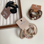 A flat lay of three sets of hair ties, including black, brown, and beige options, each with decorative beads or pearls.