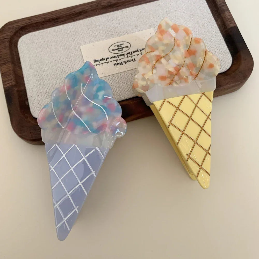 Two ice cream cone hair clips, one blue and one yellow, on a wooden tray.