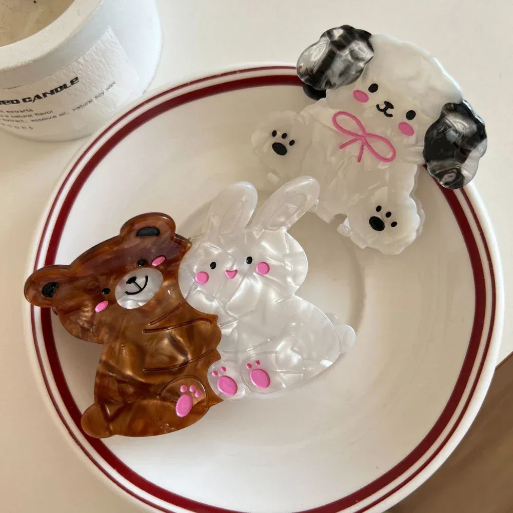 A white bunny and a brown bear hair claw clip are shown next to a white dog hair claw clip on a white plate with a red rim.