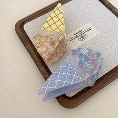 Two ice cream cone hair clips, one blue and one yellow, arranged on a tray with a card.