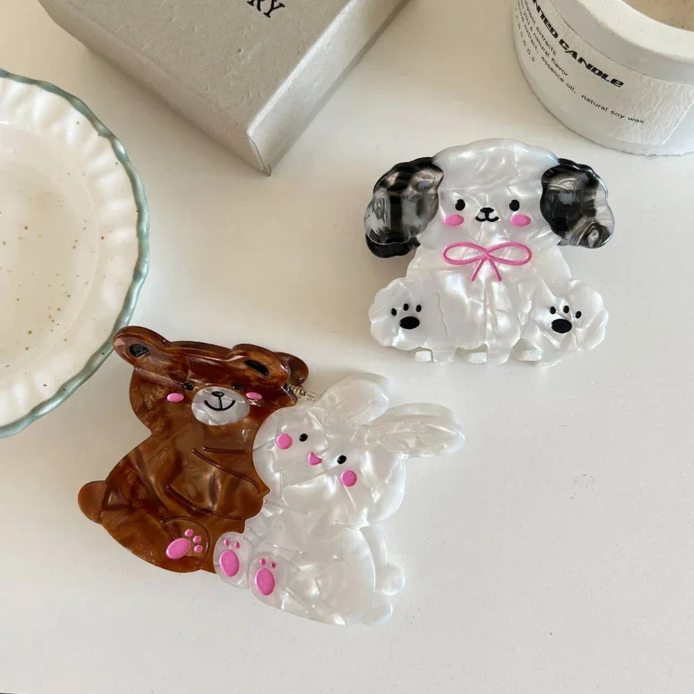 Three cute animal hair claw clips, including a bear, a bunny, and a dog, are arranged on a white surface.