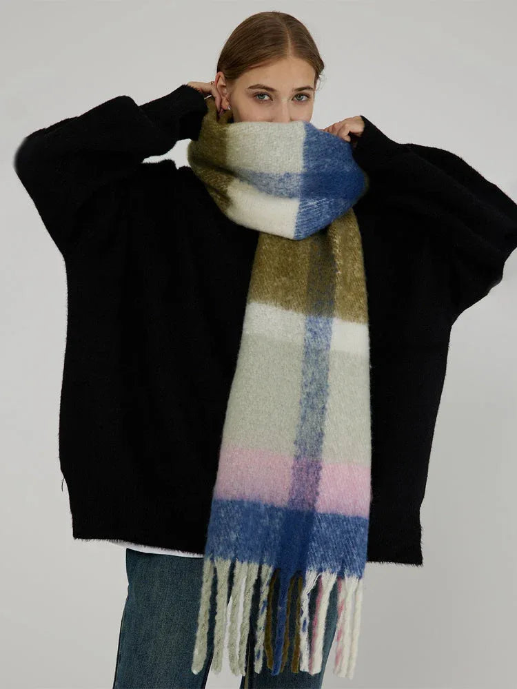Woman pulling a large plaid scarf with green, pink, blue, and white blocks up to her face.