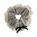 A close-up view of a black and white striped scrunchie with a lace trim and black bow.