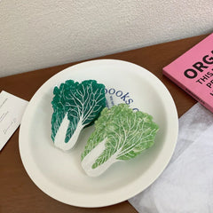 Two napa cabbage-shaped accessories, one dark green and one light green, are placed on a white plate.