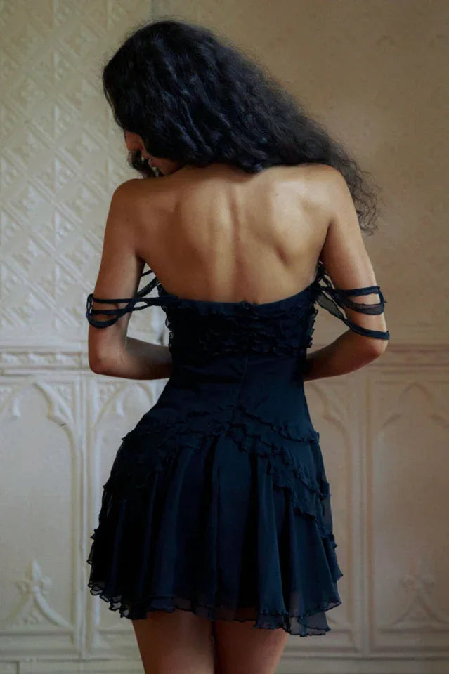 Model wearing a black strapless mini dress with ruffle trim and sheer tiered skirt, back view.