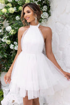 Woman wearing a white halter neck tiered tulle party dress, smiling and posing.