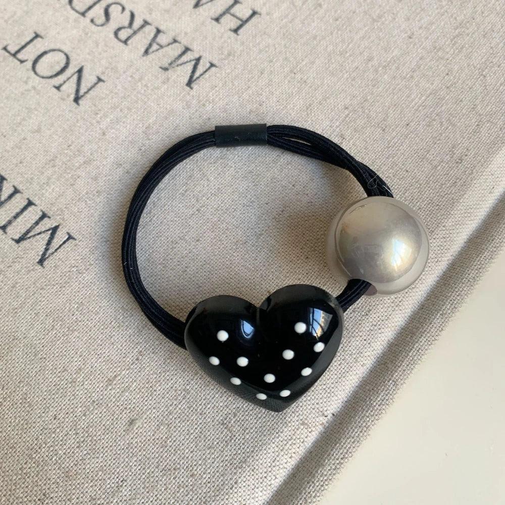 Black heart-shaped hair tie with white polka dots and a silver bead