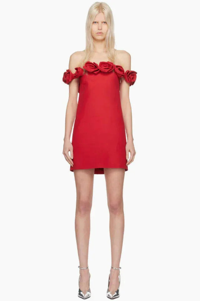 Woman wearing a red off-the-shoulder mini dress with rose embellishments on the neckline and silver strappy heels.