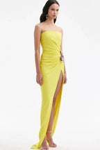 Side view of a woman in a yellow strapless gown with a high slit and floral embellishment against a white background.