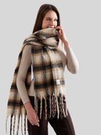 Close-up of a woman wearing an oversized plaid scarf, with her hand gently touching the scarf near her chin.