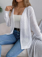 Woman in a white open-knit cardigan, white tank top, and blue jeans, seated on a couch.