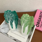 Two napa cabbage-shaped accessories, one dark green and one light green, are presented in a white box with a greeting card.