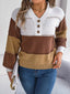 Woman wearing a brown, tan, and white color block knit sweater with a v-neck and button details, paired with blue jeans and holding a white clutch.