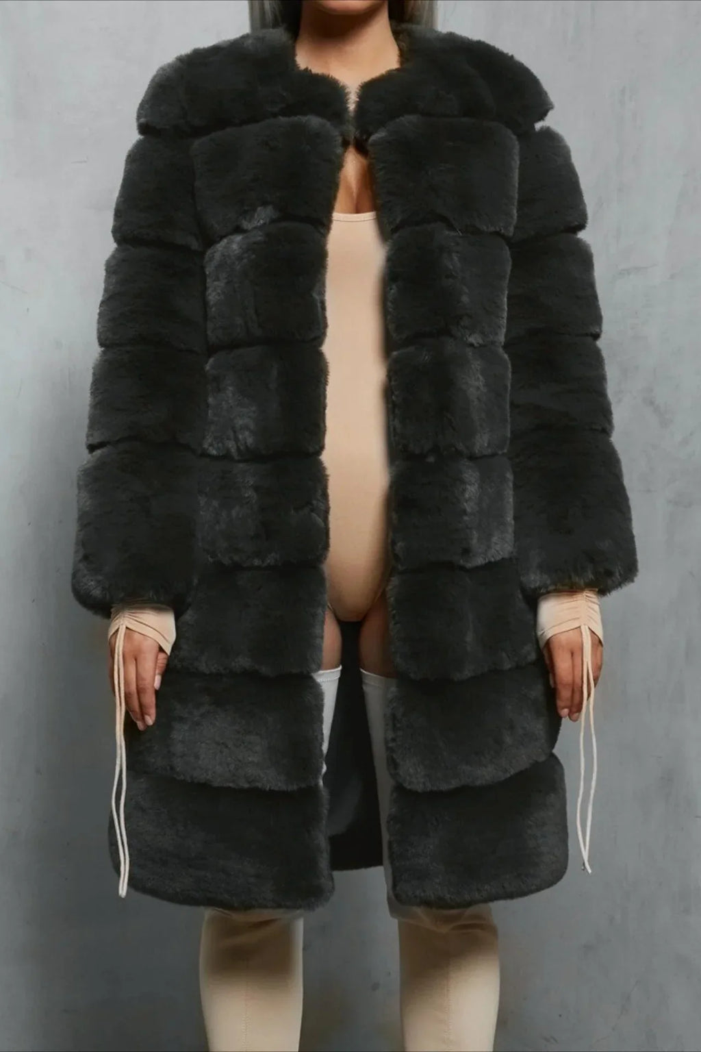 Woman wearing a dark gray faux fur coat over a beige bodysuit and thigh-high socks.