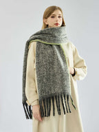 Woman wearing a long, grey, textured knit scarf with fringe detail and lime green trim, draped over a cream coat.