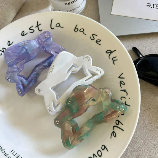 three abstract figure hair claw clips in purple, white, and marbled green/pink/brown on a white plate