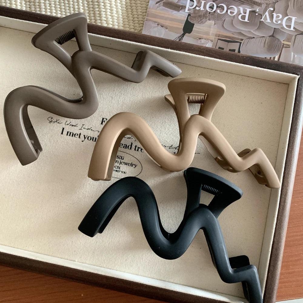 Four wavy claw clips in brown, beige, and black, displayed on a textured surface.