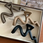 Four wavy claw clips in brown, beige, and black, displayed on a textured surface.