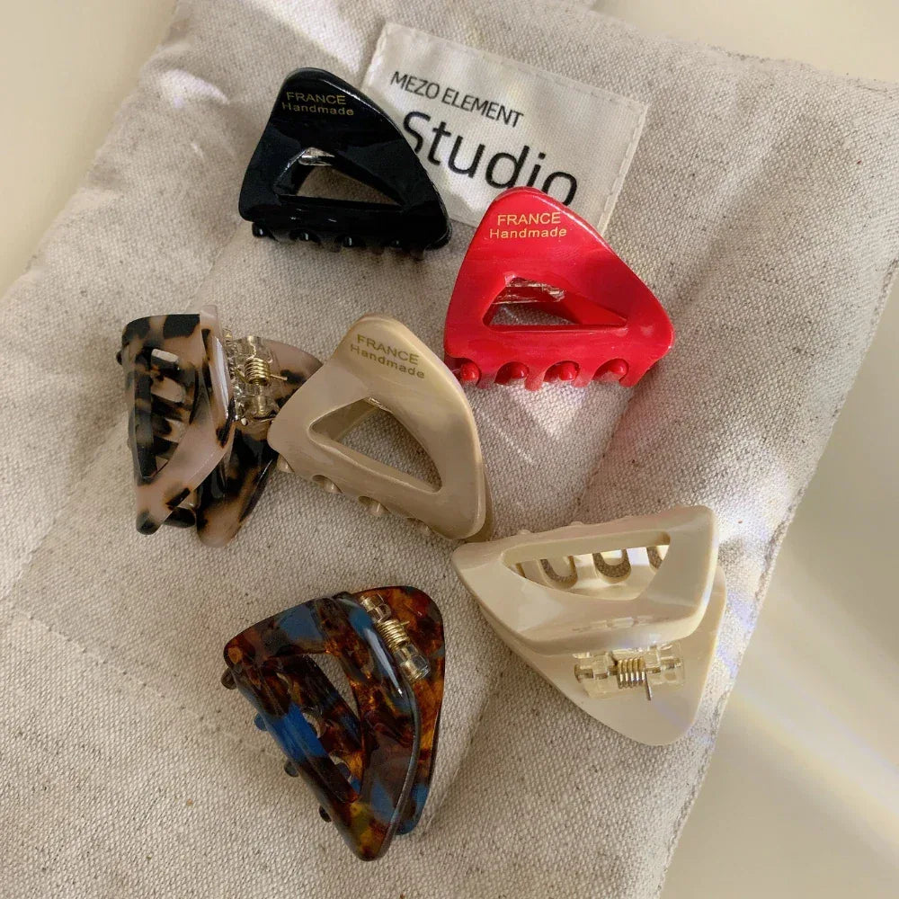 Close-up view of six triangular hair clips with differing patterns and solid colors on a neutral fabric background