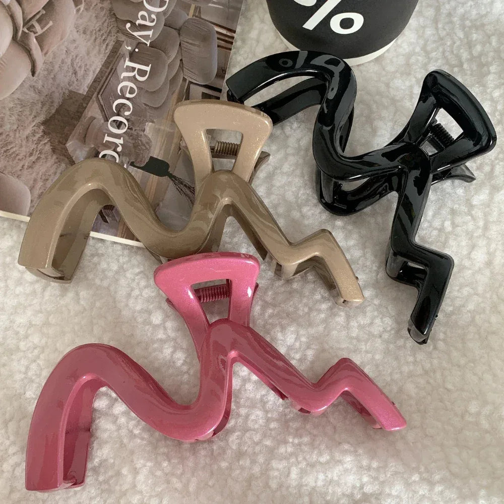 Four wavy claw clips in beige, black, and pink, arranged on a white, fluffy surface.