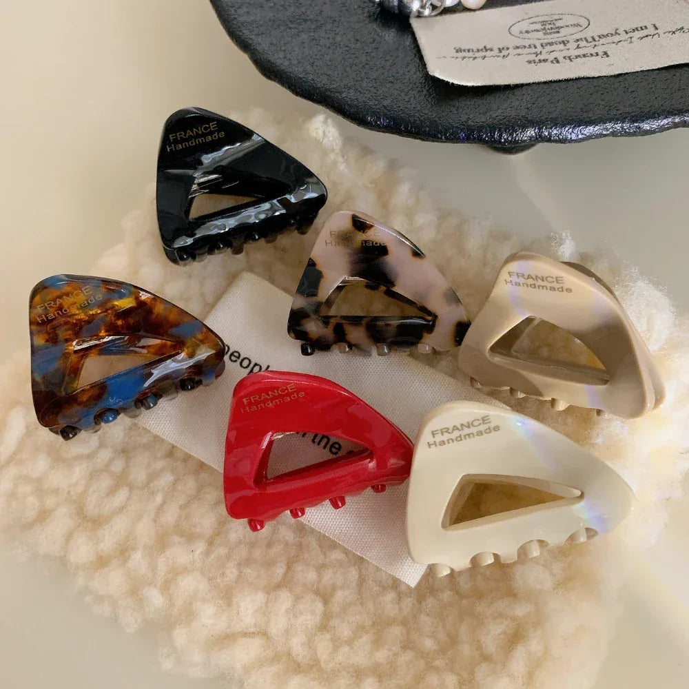 Collection of six triangular hair clips in various colors and patterns arranged on a textured fabric
