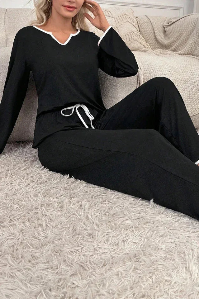 woman wearing black long sleeve pajama set with white piping, sitting on the floor