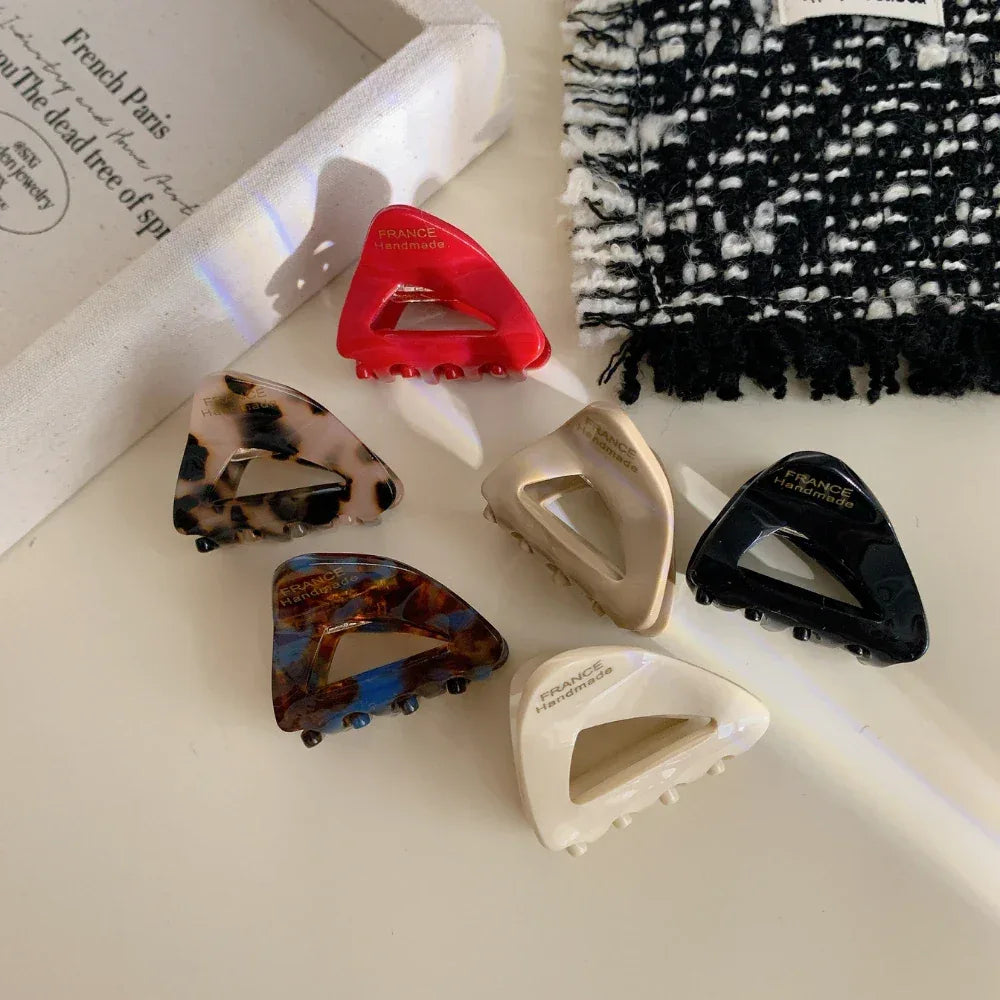 Assortment of triangular hair clips in different hues and designs, displayed on a light-colored cloth